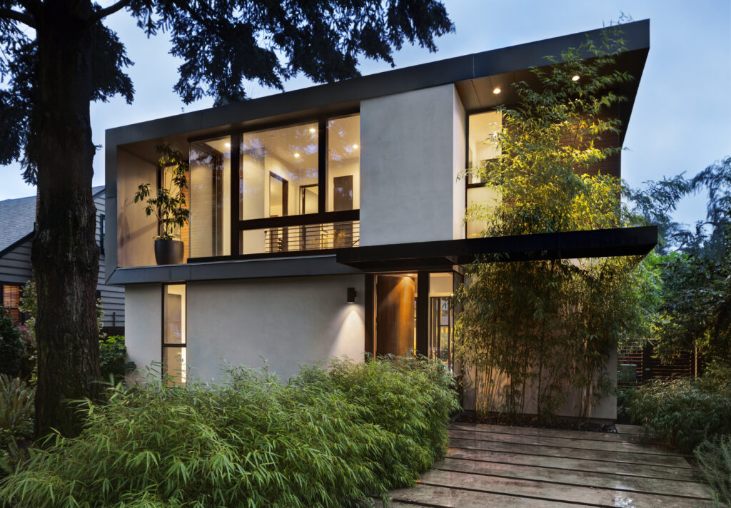 Modern home at twilight with interior and exterior lighting and lush landscaping. Open front door to well lit home interior.