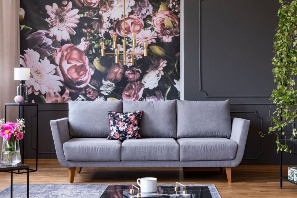 Gray couch with floral patterned pillow that matches floral wallpaper