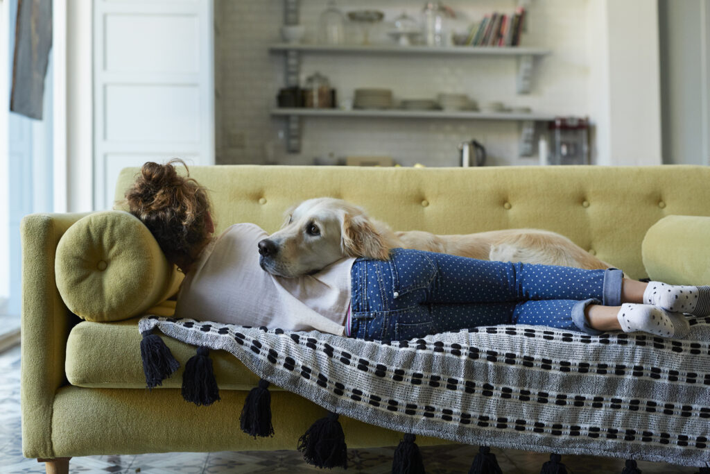 Women laying on yellow couch with her lab dog on top of her