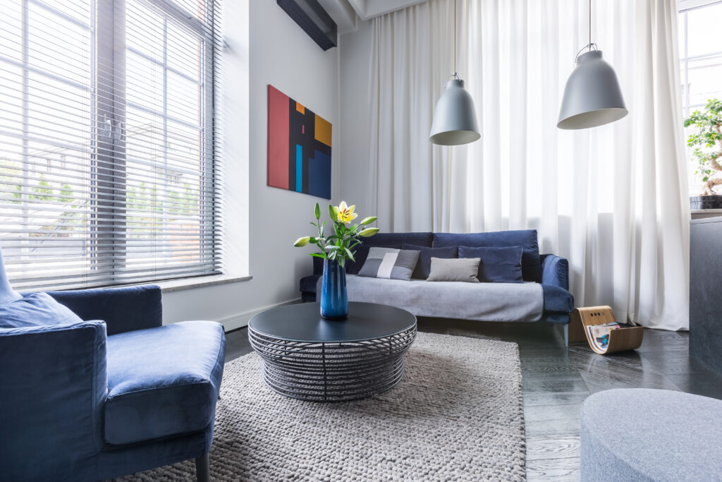 Living room with blue upholstered furniture, window blinds and white net curtain