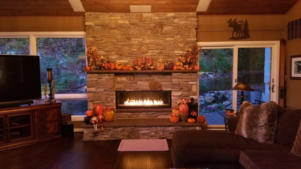 Beautiful stone mason fireplace, flames glowing at dusk, in a large rustic home-like setting, during the autumn/fall holiday timeframe. Cozy, grand, special.