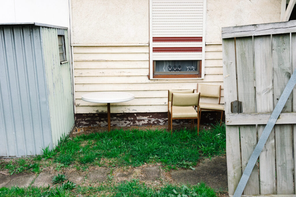 An unkept suburban backyard in Melbourne, Sutralia with rusted chairs and table an old metal shed and broken wooden door.