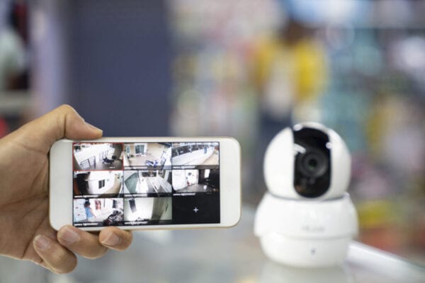 A Person's Hand Holding Mobile Phone With CCTV Camera Footage On Screen