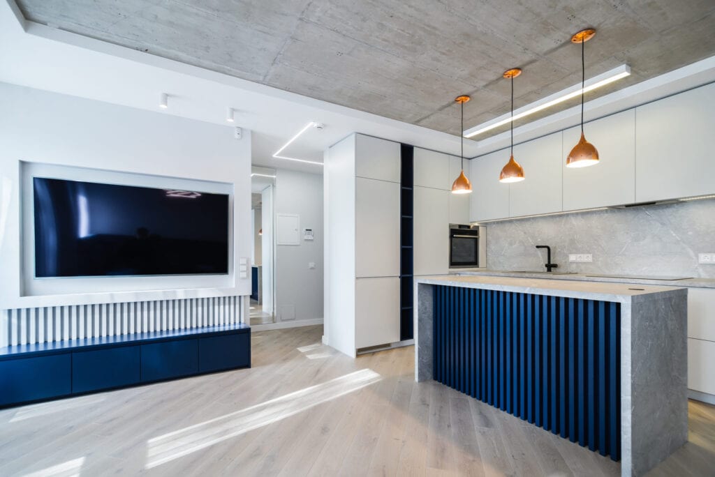 Modern and urban apartment interior with white colors, some plain concrete details and some blue colors. Living room connected with kitchen.