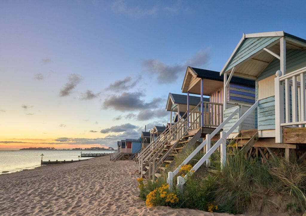 Early morning summer sunrise illuminates the row of beautifully coloured beach huts on the North Norfolk coast at Wells next the sea.