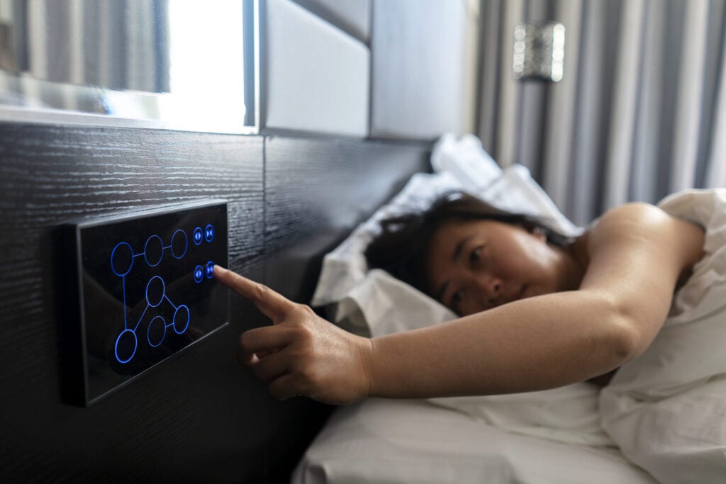 woman sleeping on bed, pushing button to open curtain, in a smart hotel