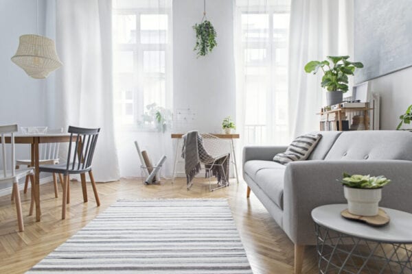 Modern scandinavian living room with design furniture, family table, plants, bamboo bookstand and wooden desk. Brown wooden parquet. Abstract painting on the white wall. Nice apartment.