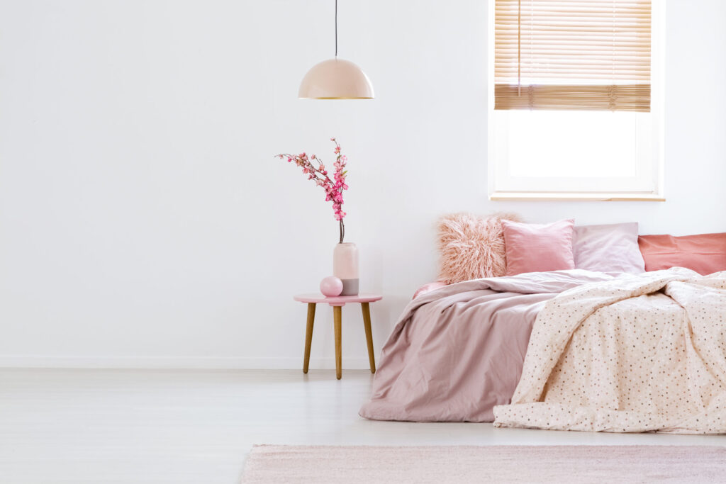 Lamp above table with flowers in pink pastel bedroom interior with window above bed. Real photo