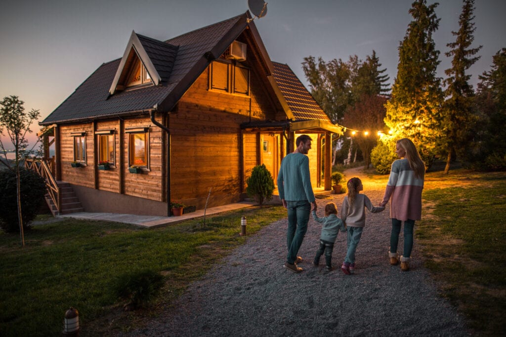 Back view of young smiling parents holding hands with their children and walking in nature in the evening.