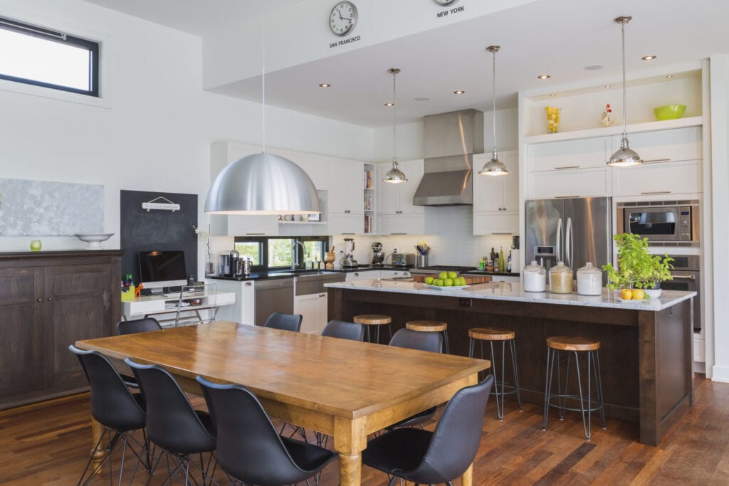 Open-concept dining and kitchen area with antique dining table with black leather and plastic chairs, marble top wooden island with painted black steel and exotic wood barstools, white cabinets inside a luxurious modern cube style house, Quebec, Canada. This image is property released. CUPR0343