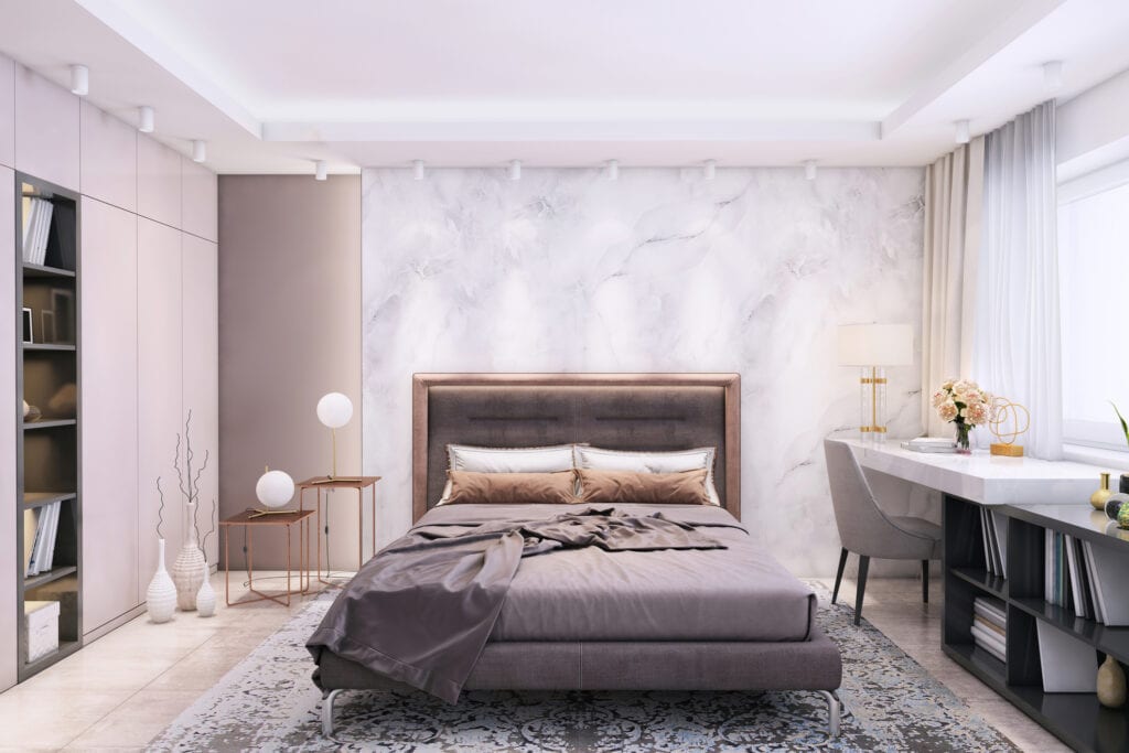 Modern bedroom interior with large pastel colored bed and pillows with big blank marble wall for copy space in the background.