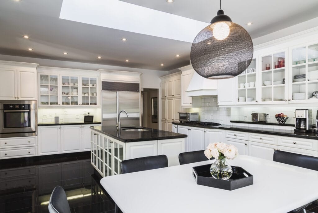 White breakfast table with black leather chairs, white wood and glass pane island with black granite countertop and cupboards in country style kitchen with black granite tile flooring inside a 1924 semi-detached cottage style home, Quebec, Canada. This image is property released. CUPR0358