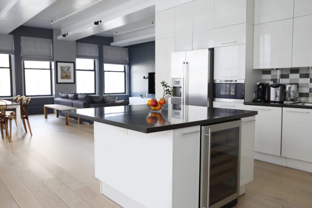 Interior view of modern kitchen and living room, with white cabinets in loft apartment.