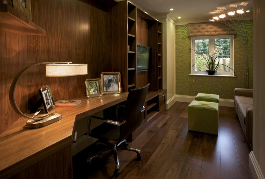 A beautiful dark-wood paneled office room in a luxury penthouse apartment. The flooring is made from solid walnut. This is a show home for a luxury development and has been furnished by an interior designer. Two green footstool cubes are illuminated by an unusual corner lamp unit. A large desk lamp illuminates the desk top. All framed images are included in my iStock portfolio.