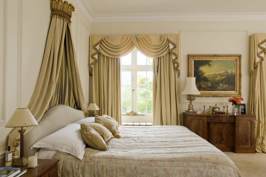 Bed with gilt coronet in bedroom with full length pale gold curtains, Ampney Park, 17th century english country house