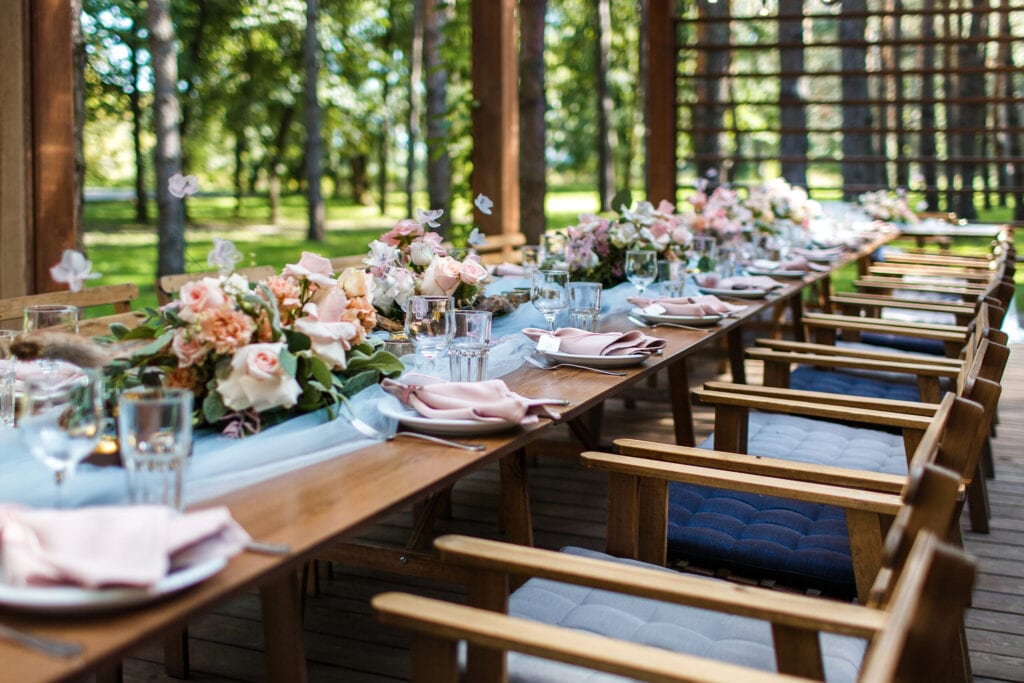 A plates with a light pink napkins are on the table. Nameplate.The table is decorated with gray-blue tulle.Also decorated with flower-wooden compositions, bronze candlesticks, simple glasses.Fine art