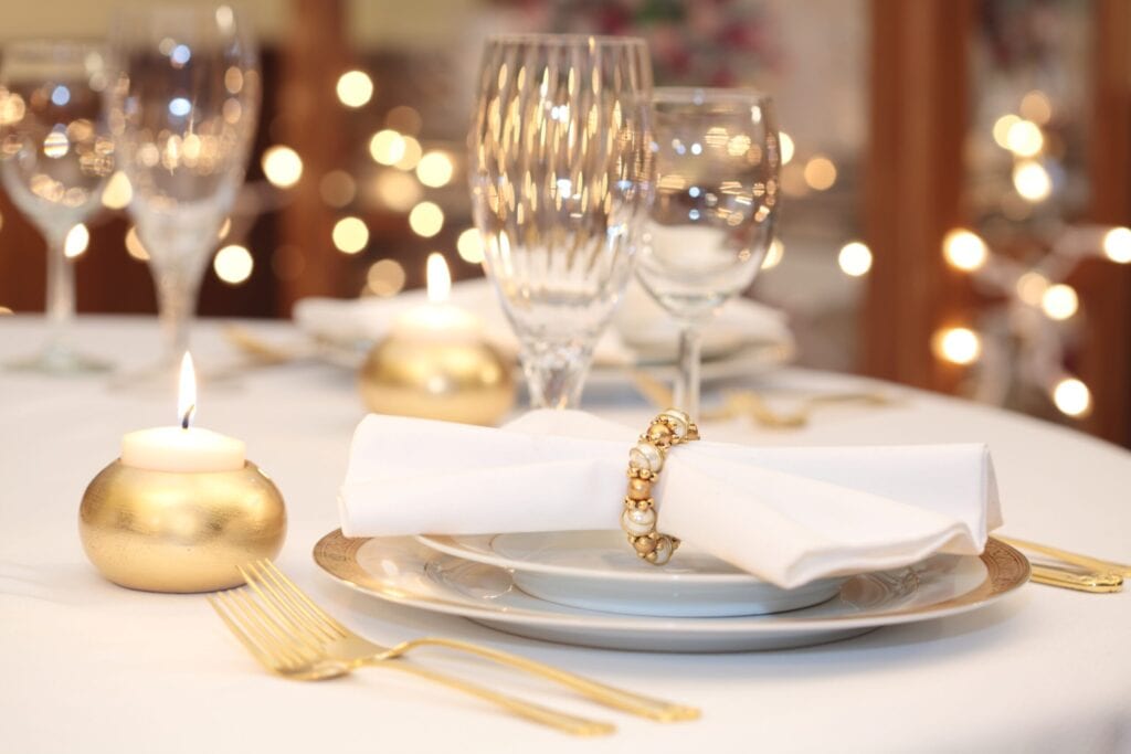 Elegant place setting in gold, white and clear crystal. Gold candle holder with burning candle. Lights in background are out of focus. Shallow depth of field.