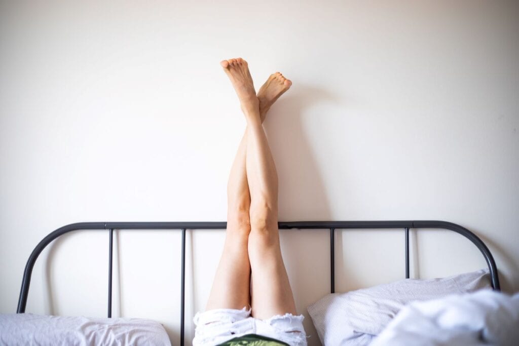 Woman with legs kicked up against wall and metal headboard