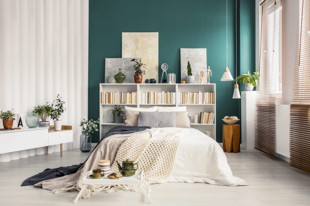Bedroom with green accent wall, book shelf is being used as headboard