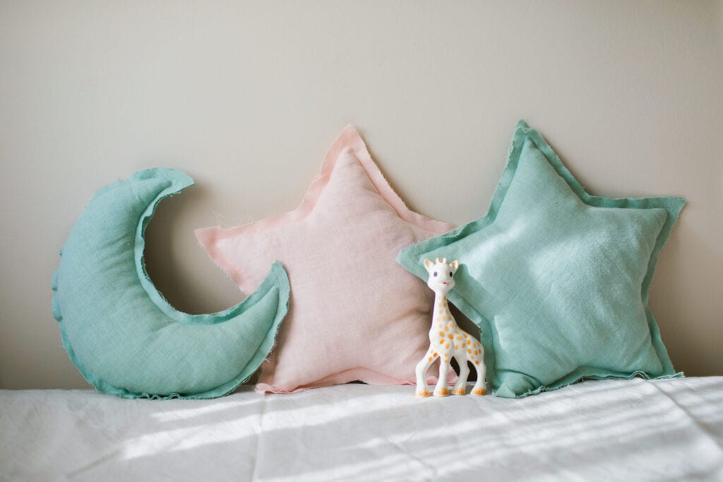 Linen blue and pink moon and star pillows toy on light bedding over beige background. Decorative baby cushions on nursery.