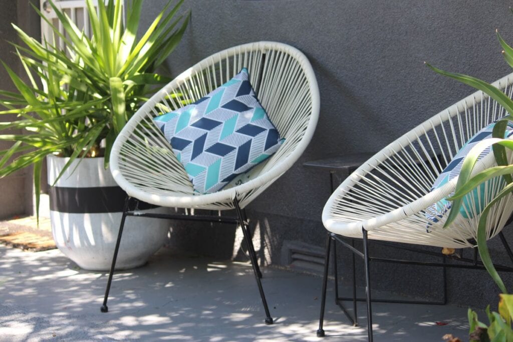 Two white acapulco chairs with colorful geometric pillows
