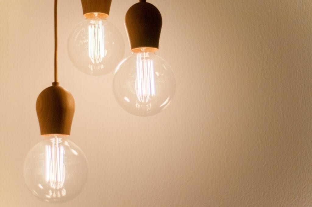 Three lit-up lightbulbs hanging by cords on a beige background.