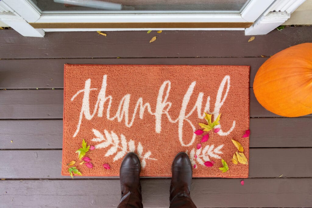Welcome mat on the front porch with the word "thankful" with boots and fall leaves