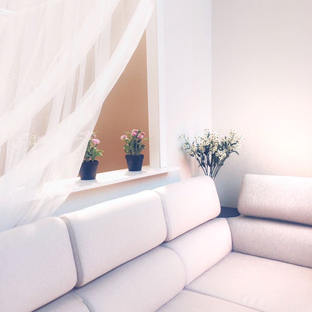 The white color of the couch, walls, and curtains creates harmony and unity in the home