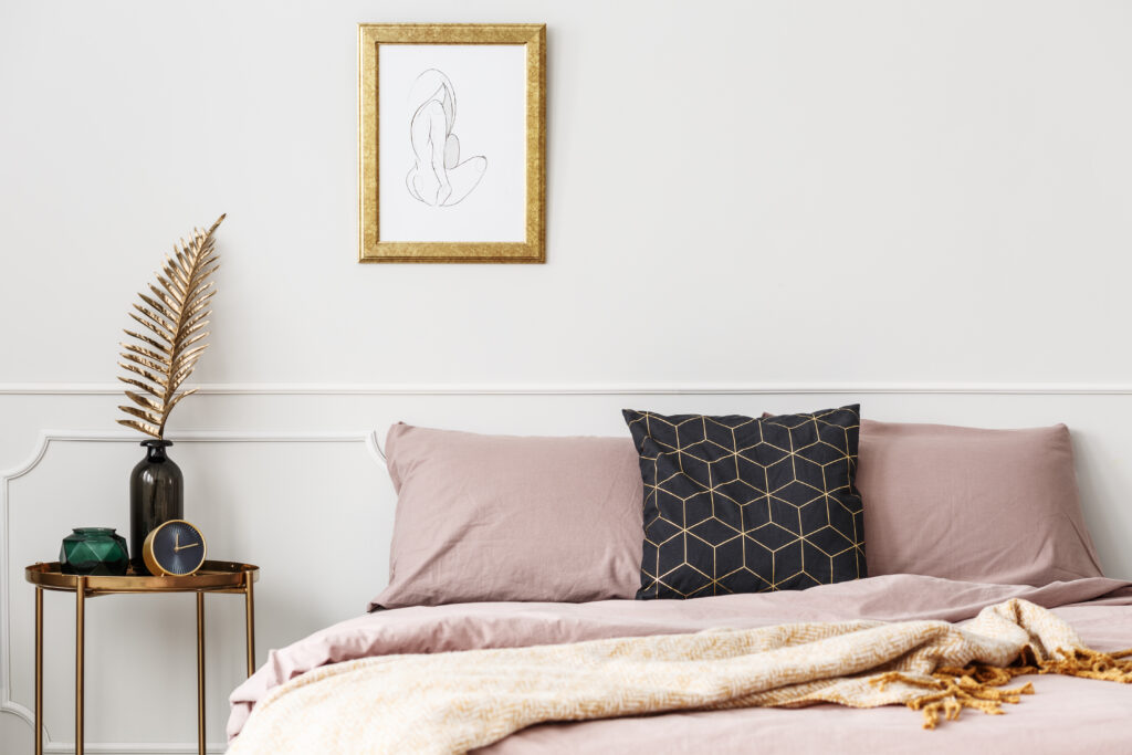 Framed sketch hanging above bed with dirty pink bedding and black cushion with golden pattern