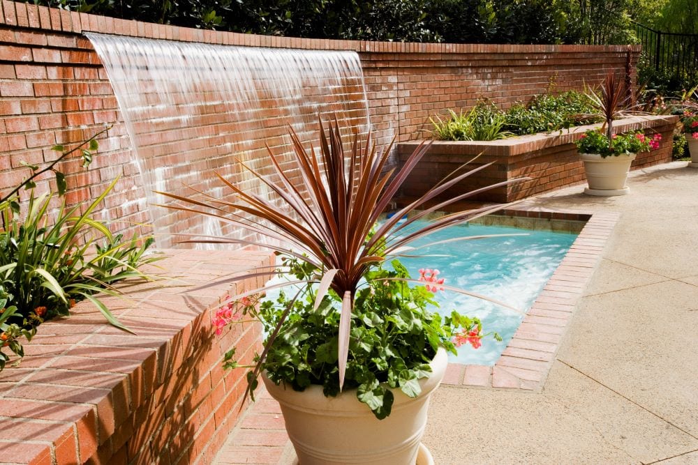 Waterfall created from brick wall flowing into backyard pond