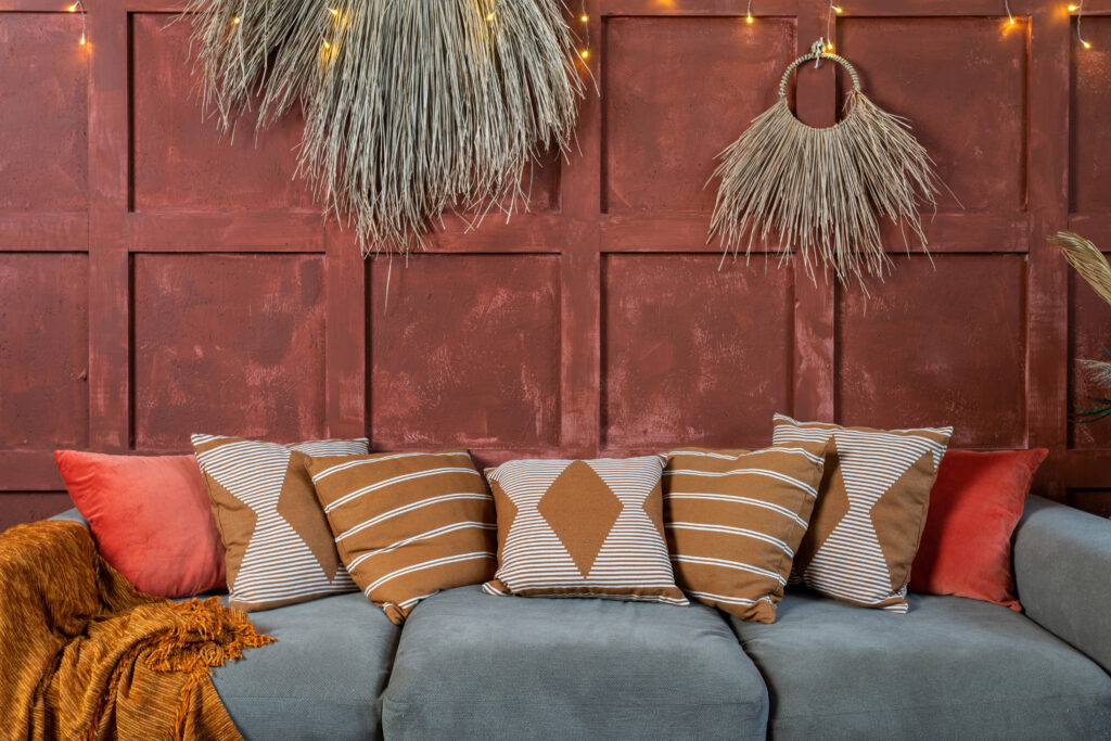 Elements of cozy room with boho style interior, couch or sofa and pillows, cushions near decoration plant composition on orange wall