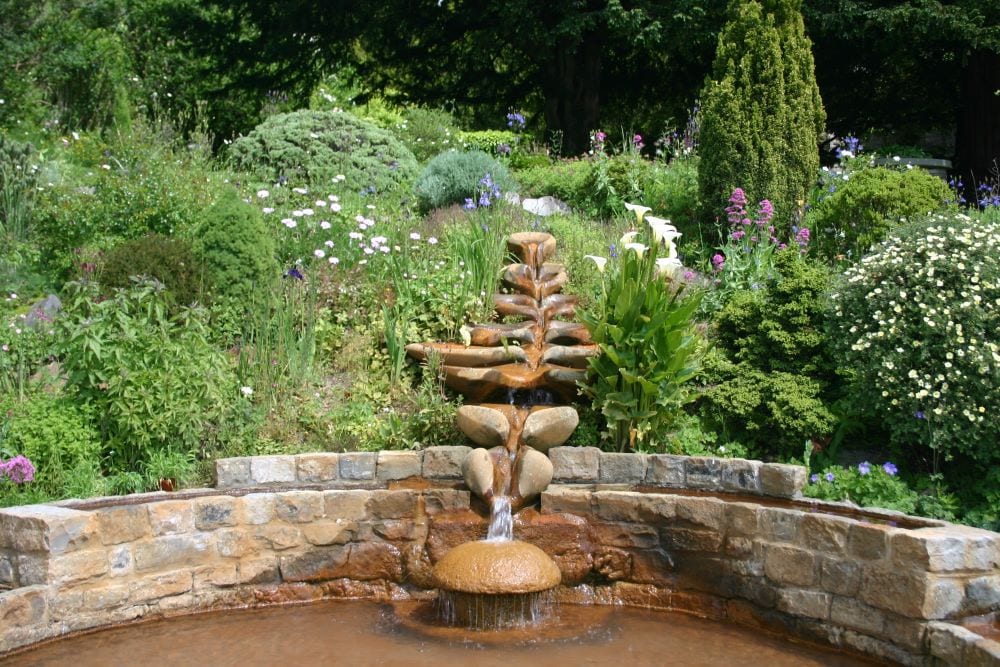 Garden waterfall created from brick and rocks, surrounded by lush green landscaping