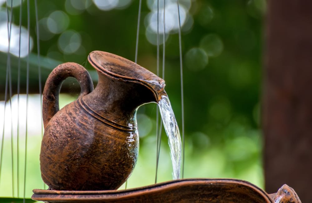 Copper clay water jug creating waterfall in garden