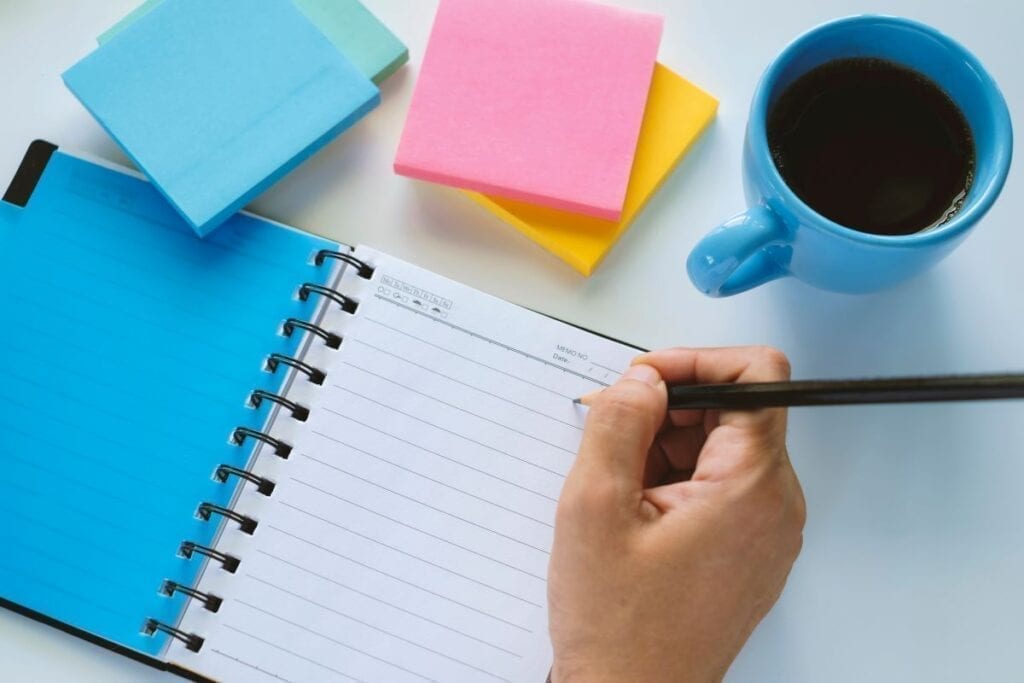 Person writing checklist or to do list in notebook and sticky notes