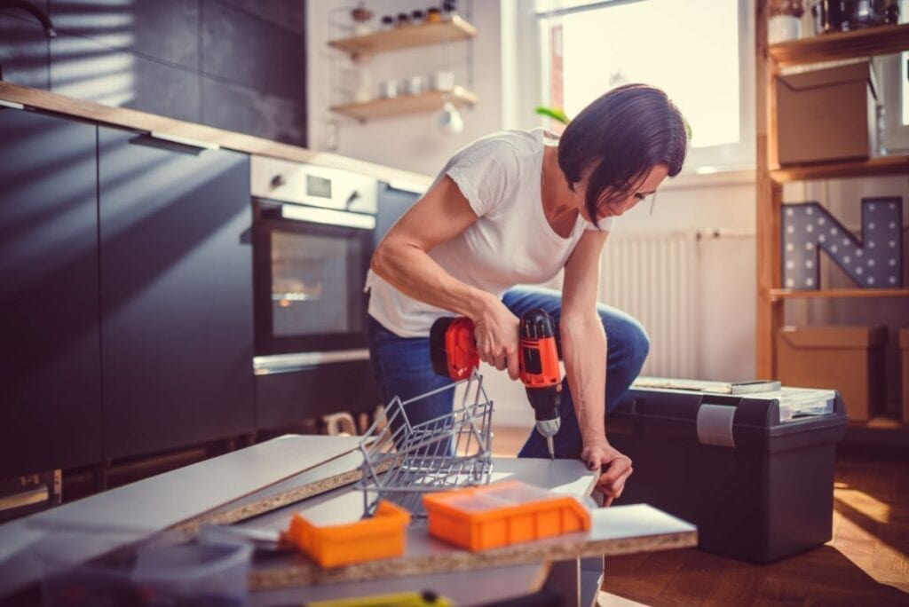 Woman is drilling wood to remodel her own kitchen in a DIY project