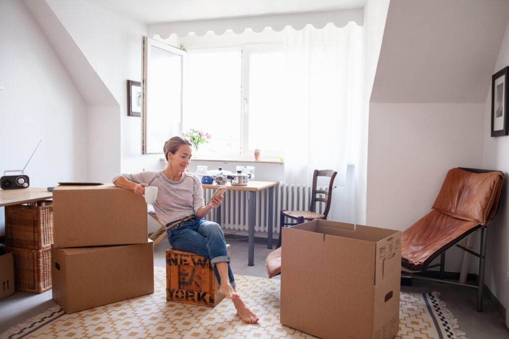 Woman in packed apartment sitting on moving box