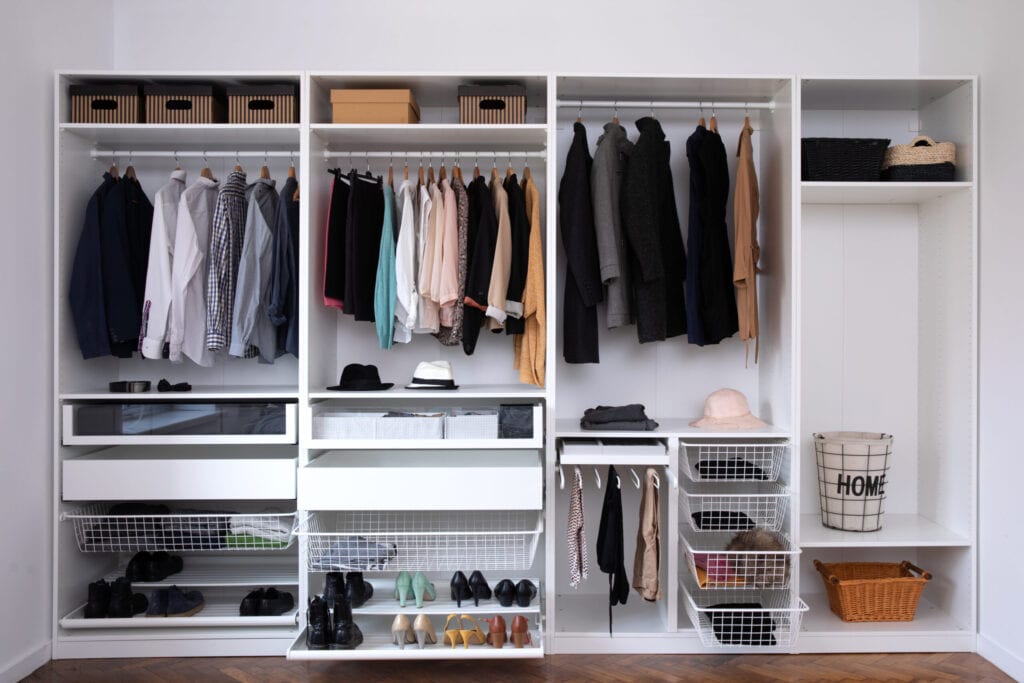 Stylish clothes, shoes and home stuff in large wardrobe closet. Dressing room interior with big wardrobe