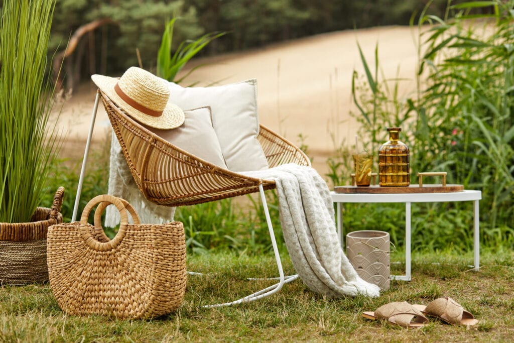 Stylish composition of outdoor garden on the lake with design rattan armchair and elegant accessories. Summer chillout mood.