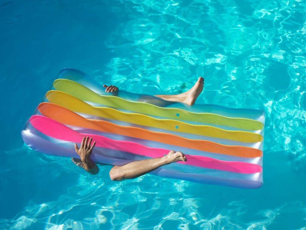 Man laying underneath rainbow pool float