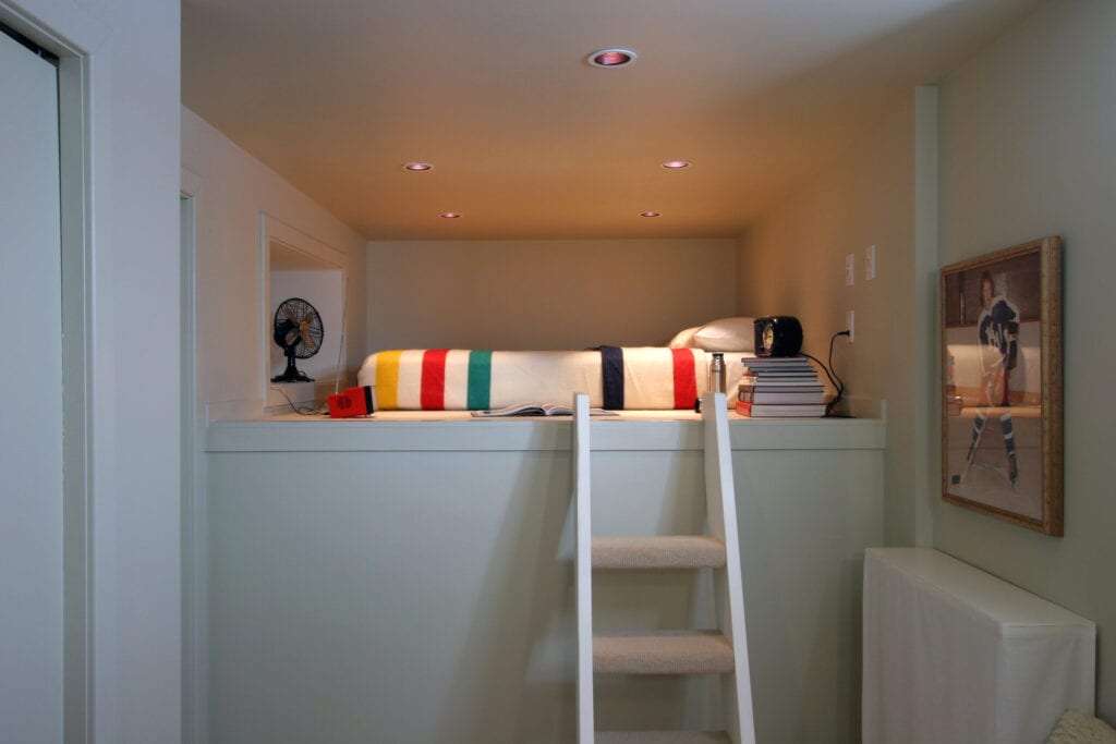 Minimally designed white loft bedroom. The room features a bed with a bright Hudson's Bay Blanket as well as red and black accent pieces.