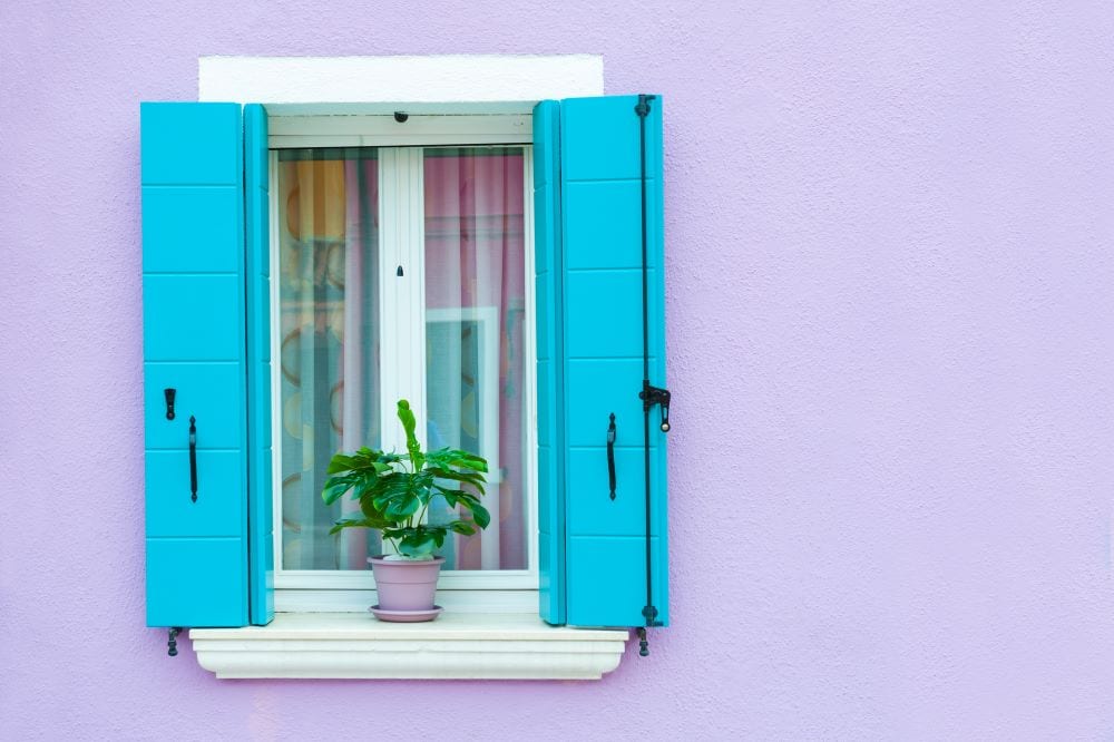 Close up of window with blue shutters against lavender wall