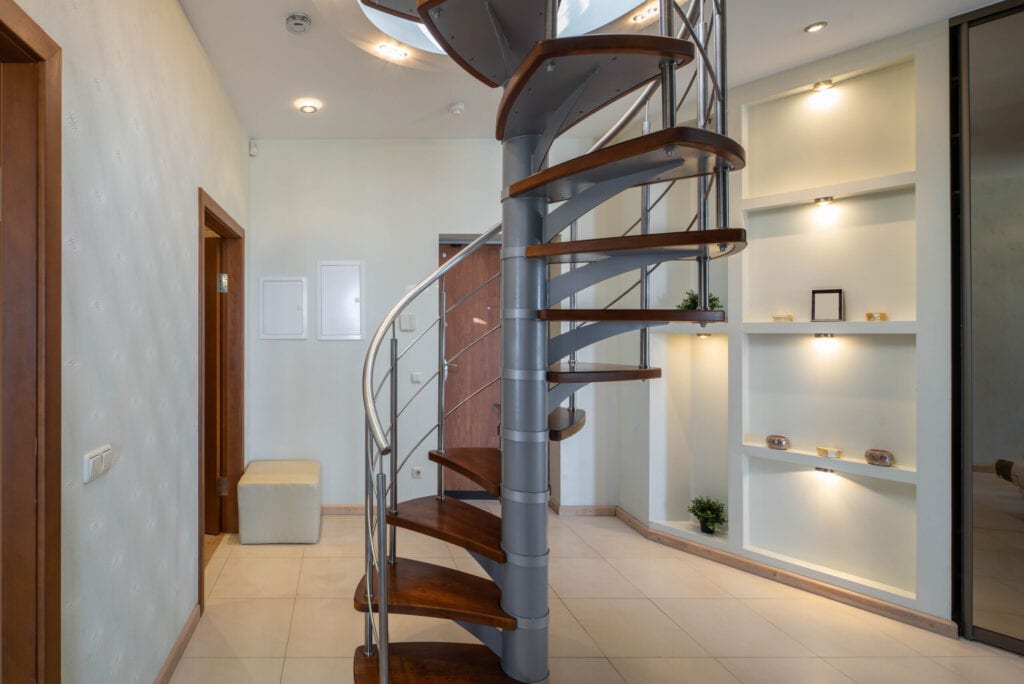 Entrance door and hall in luxury apartment. Spiral staircase. Modern interior in light tones.