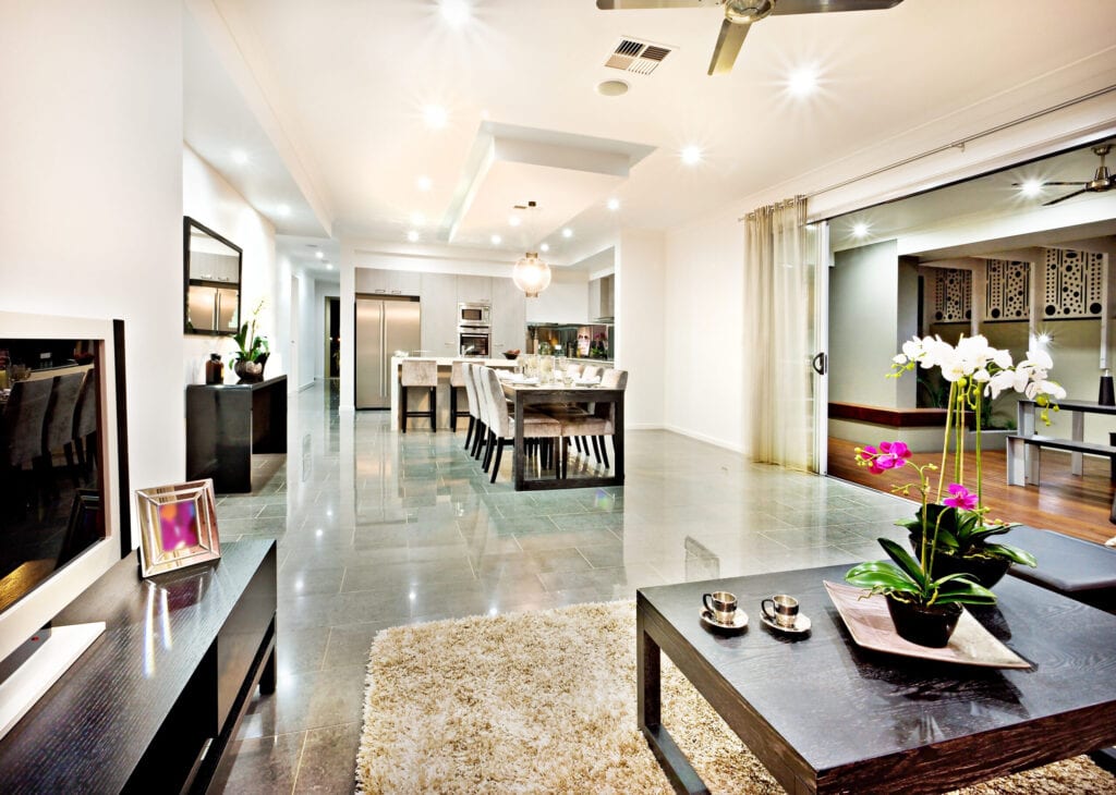 Luxurious living room with black benches and a table with a fancy flowering plant and green leaves beside the door entrance, the long hallway with tile floor go the dining and kitchen area