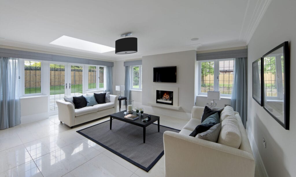  a gorgeous lounge in an expensive new home with two cream coloured settees on either side of a coffee table with a lit gas fire in the background. Subtely decorated with light blue drapes and matching cushions. The copyright for the book design belongs to the photographer.