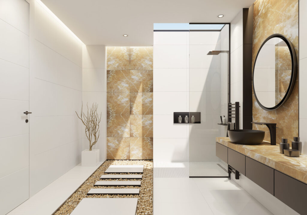 Luxurious bathroom with a skylight and natural, polished, gold onyx wall tiles, large and narrow white matte ceramic tiles and black details. long vanity unit with natural, polished, gold, onyx finish, wooden black drawers and round black ceramic washbasin, stainless steel waterfall vanity sink faucet and a decorating round mirror with black frame above. under a skylight is a walk-in shower with white matte large and long narrow, ceramic tiles, stainless steel, black shower panel,decorating wall black shelf floor with decorative golden pebbles and white matte ceramic tiles. branches in a white floor vase as a decoration.ceiling with strip cove lighting and embedded spotlights.