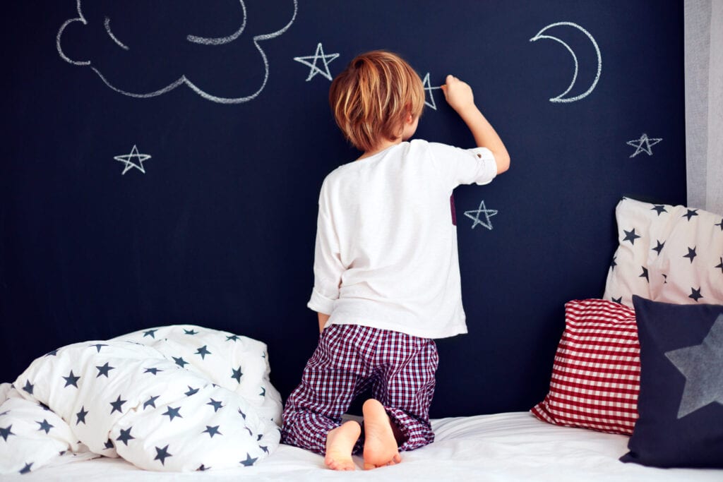 cute kid in pajamas painting chalkboard wall in his bedroom