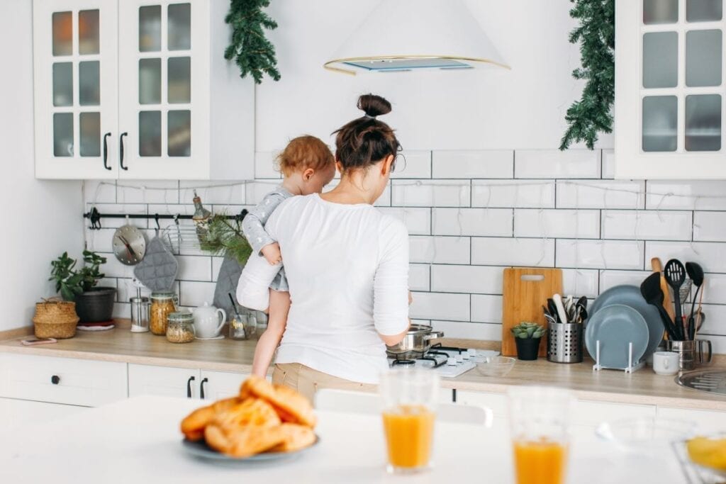 Mom holding baby and cooking breakfast in modern kitchen