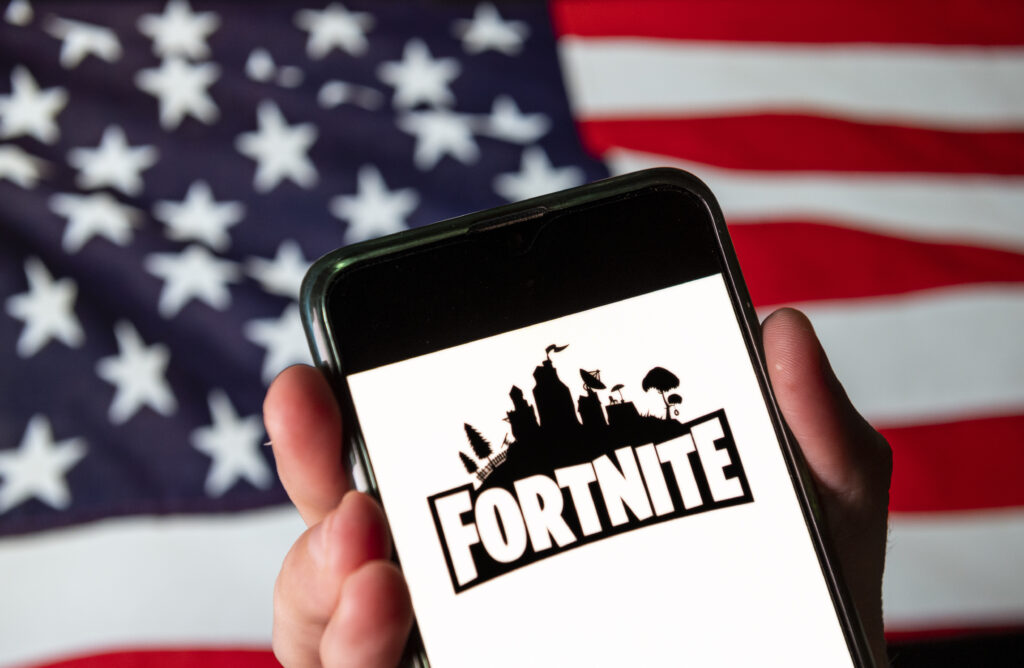 CHINA - 2020/08/15: In this photo illustration the online video game by Epic Games company Fortnite logo is seen on an Android mobile device with United States of America flag in the background. 