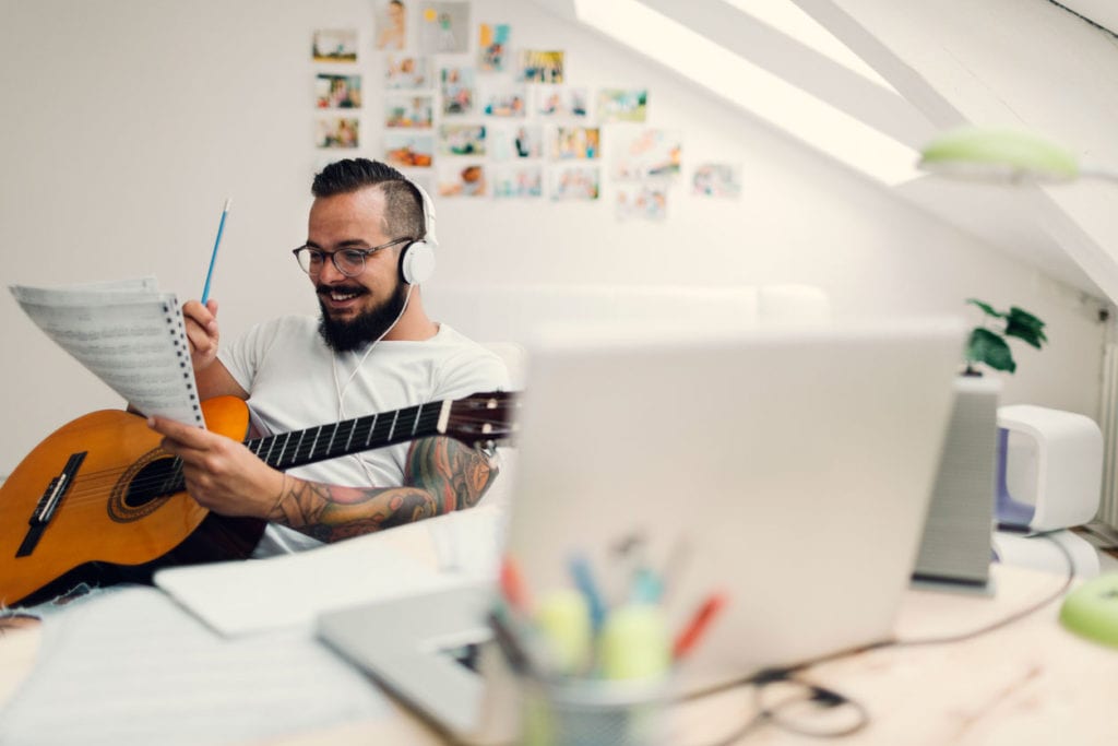 man sitting in a room smiling, playing the guitar and reading sheet music