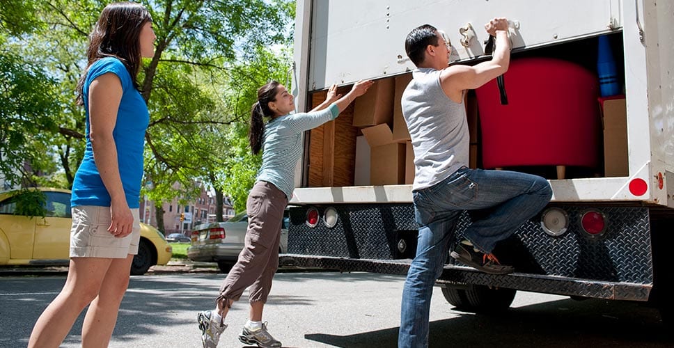 Young people close the back door of a rented moving truck.